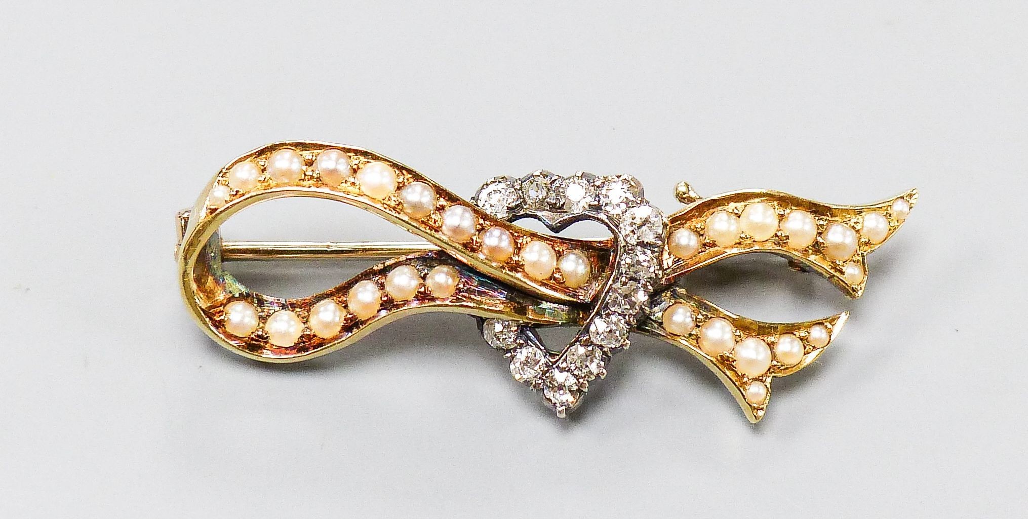 An early 20th century yellow metal, seed pearl and rose cut diamond ribbon and heart brooch, 37mm, gross weight 4.5 grams.